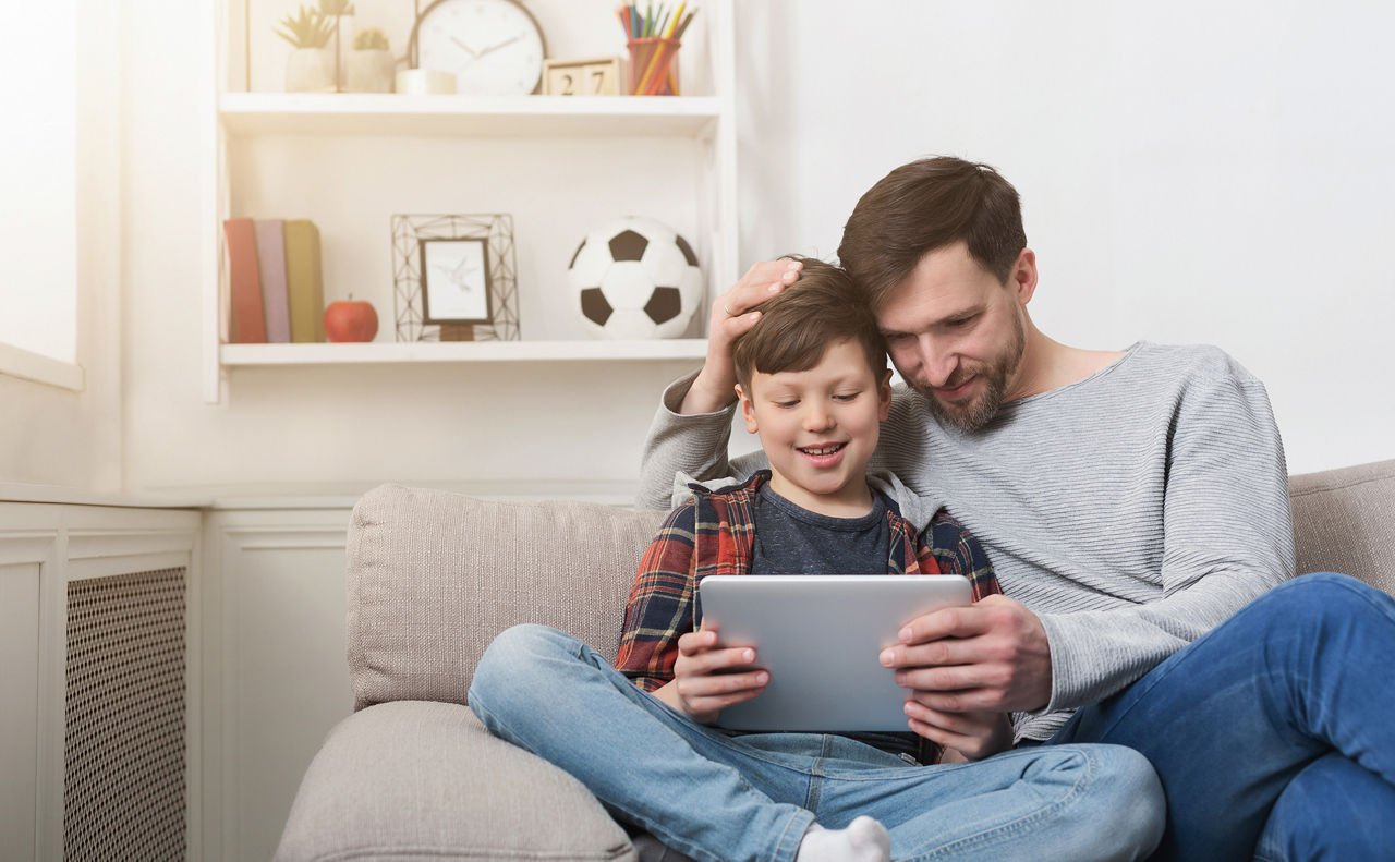 Vater und Sohn sitzen auf einem Sofa und schauen auf ein Tablet
