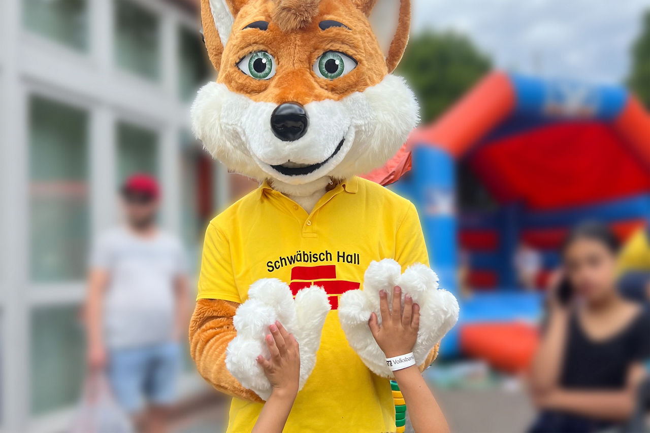 Bausparfuchs macht "High Five" mit einem Kind.