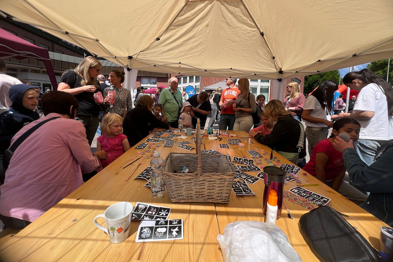 Tisch mit Erwachsenden und Kindern, die sich Glitzertattoos anbringen.