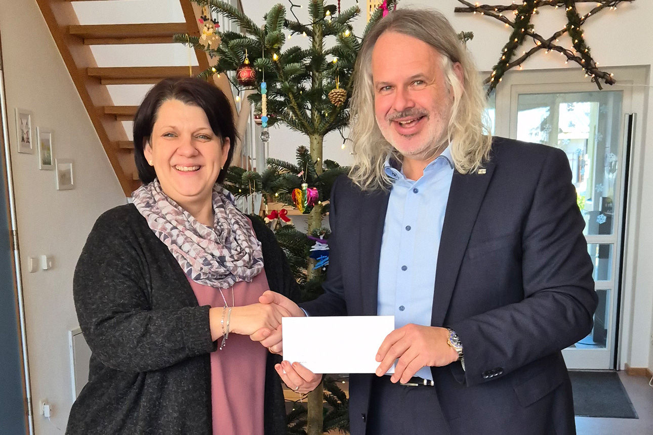 Eine Frau und ein Mann lachen in die Kamera. Sie halten einen Briefumschlag in der Hand.