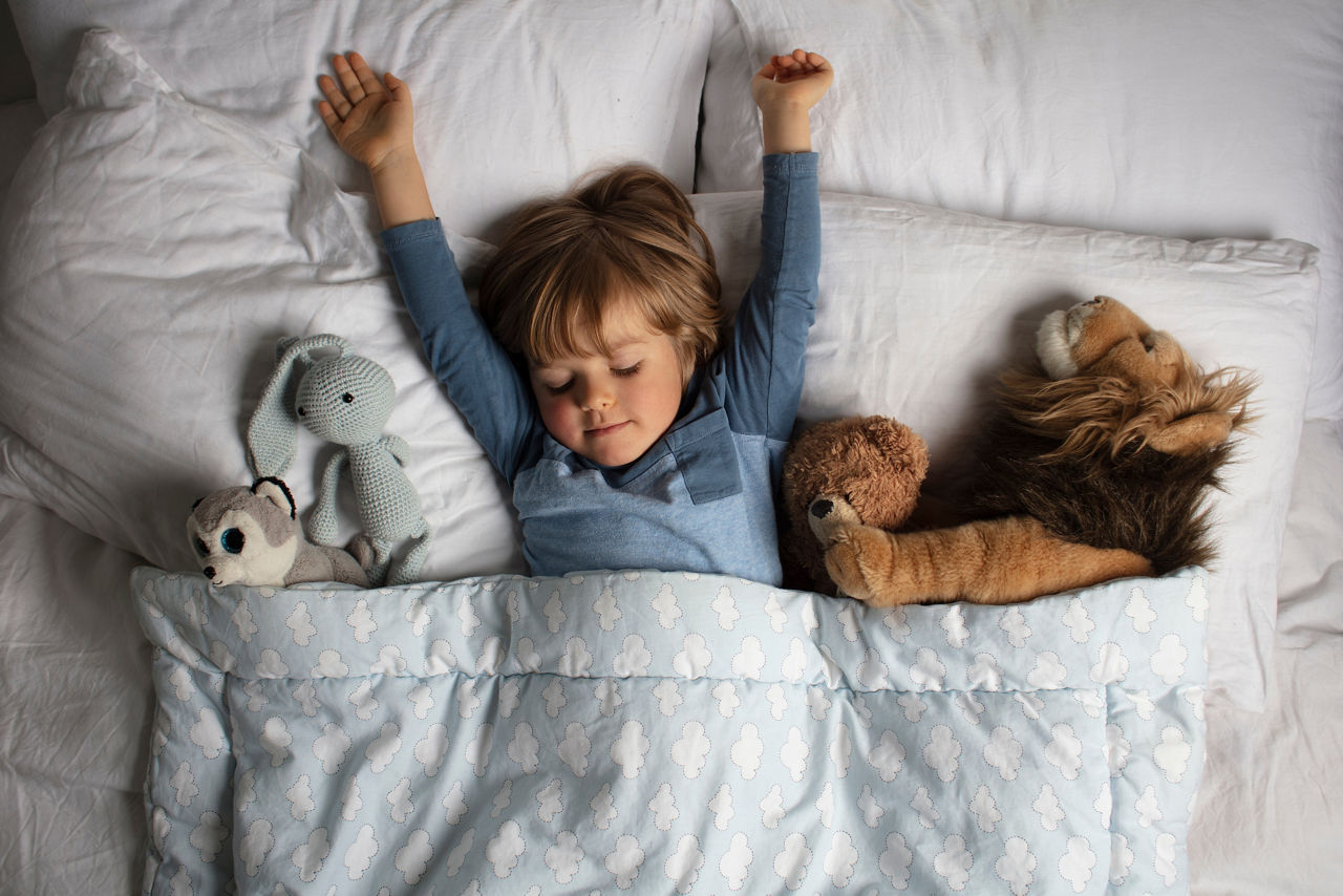Kleiner Junge schläft mit Kuscheltieren im Bett