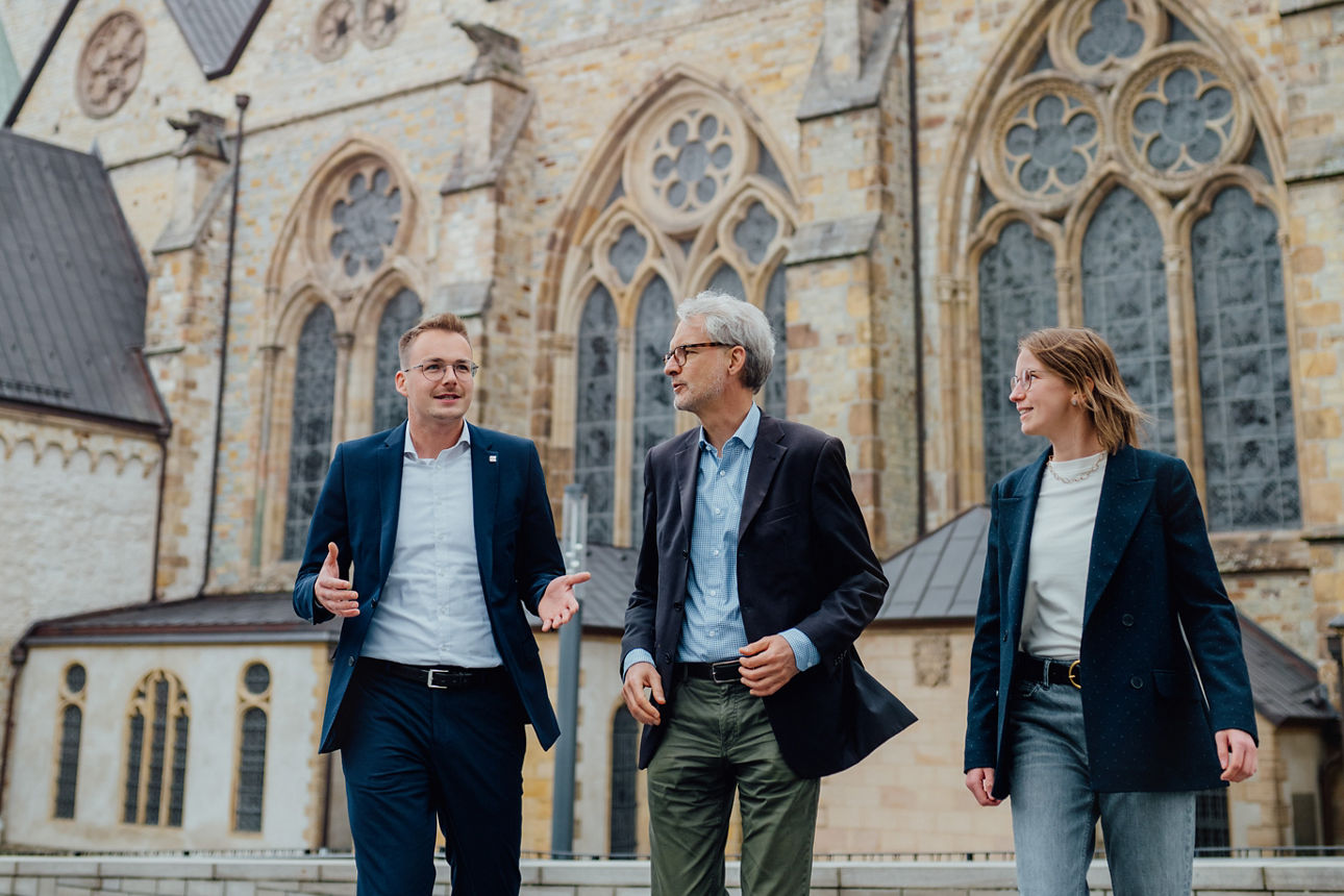 Drei Mitarbeitende stehen vor einer Kirche
