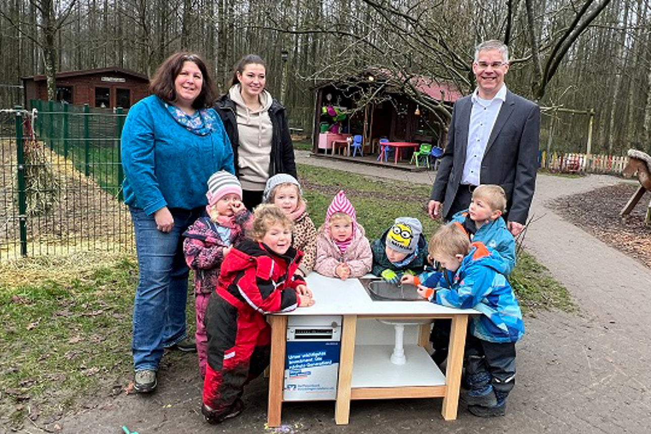 Gruppe von Kindern, Erzieherin und Vorstand an der Matschküche