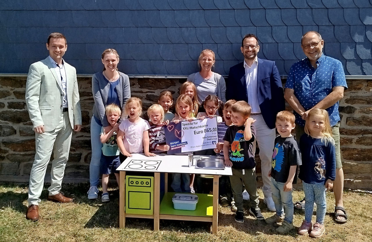 Vier Erwachsene und ein paar Kinder stehen hinter einer Matschküche für Kinder.
