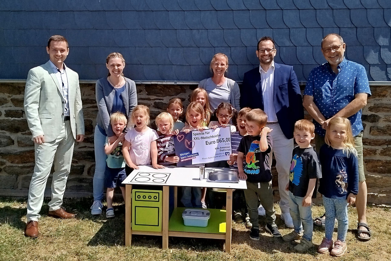 Vier Erwachsene und ein paar Kinder stehen hinter einer Matschküche für Kinder.