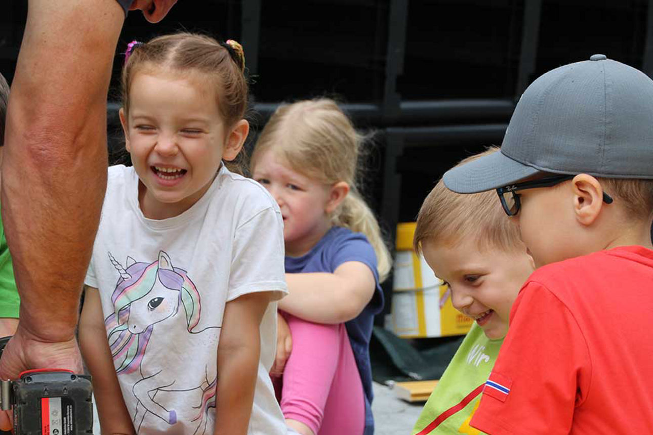 Vier Kinder sitzen auf dem Boden um die Bretter des Hochbeets. Man sieht eine Hand mit einem Akkuschrauber .