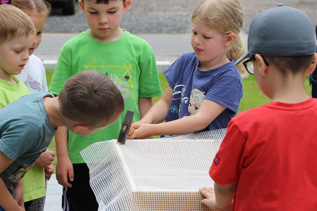 Ein Mädchen befestigt einen Stoff an einem Hochbeet. Sie schlägt mit einem Hammer einen Nagel in das Holz.