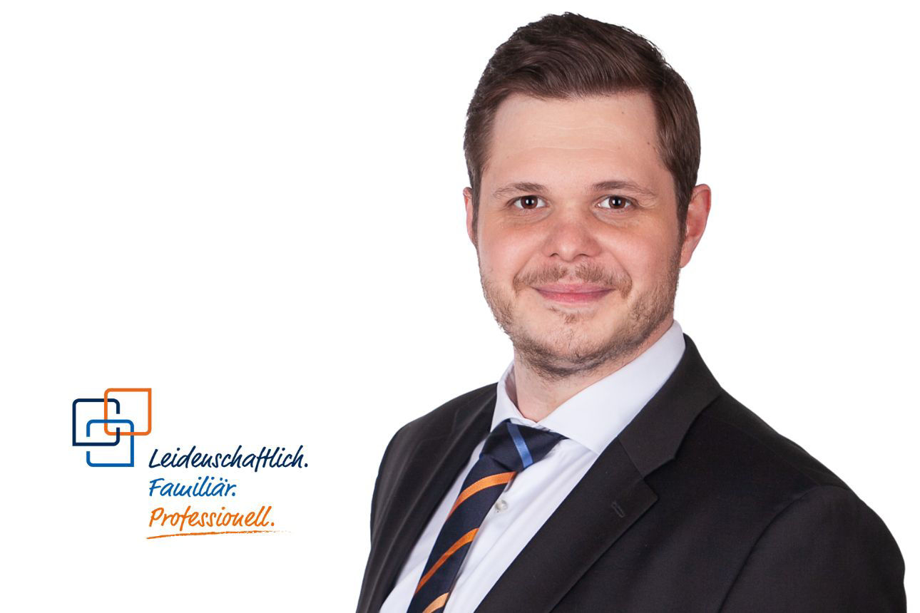 Porträt von Maximilian Klaar, lächelnd, mit Bart und einer dunkelblau-orange gestreiften Krawatte.