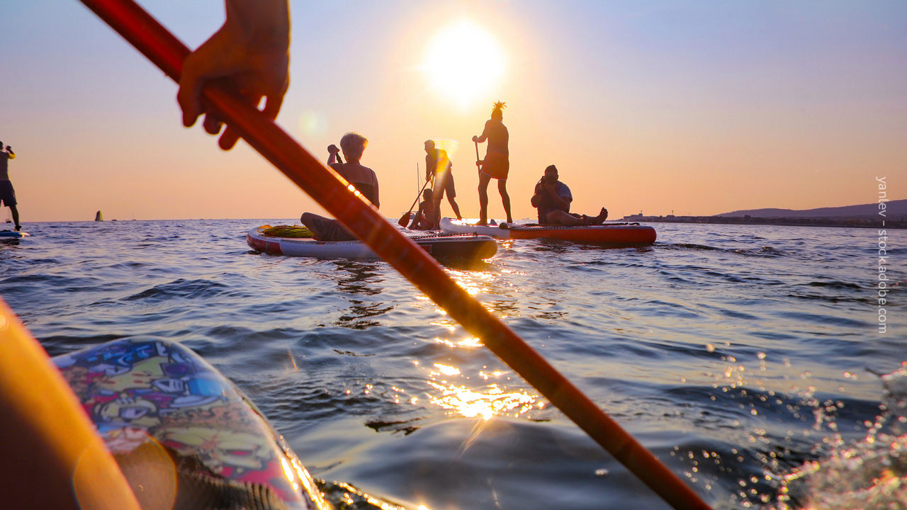 Jugendliche sitzen oder paddeln auf einem SUP auf dem Meer beim Sonnenuntergang 