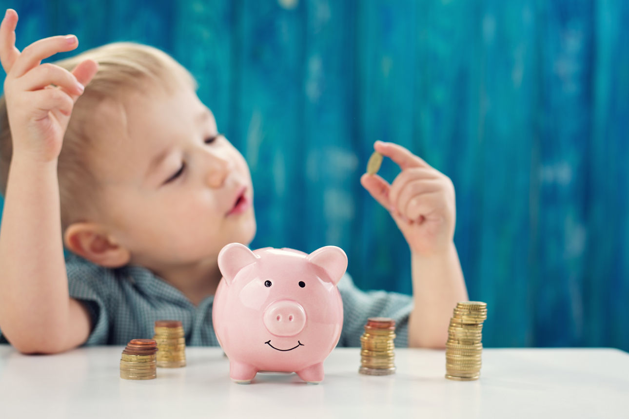 Kleiner Junge sitzt am Tisch mit Sparschwein und Münzen.