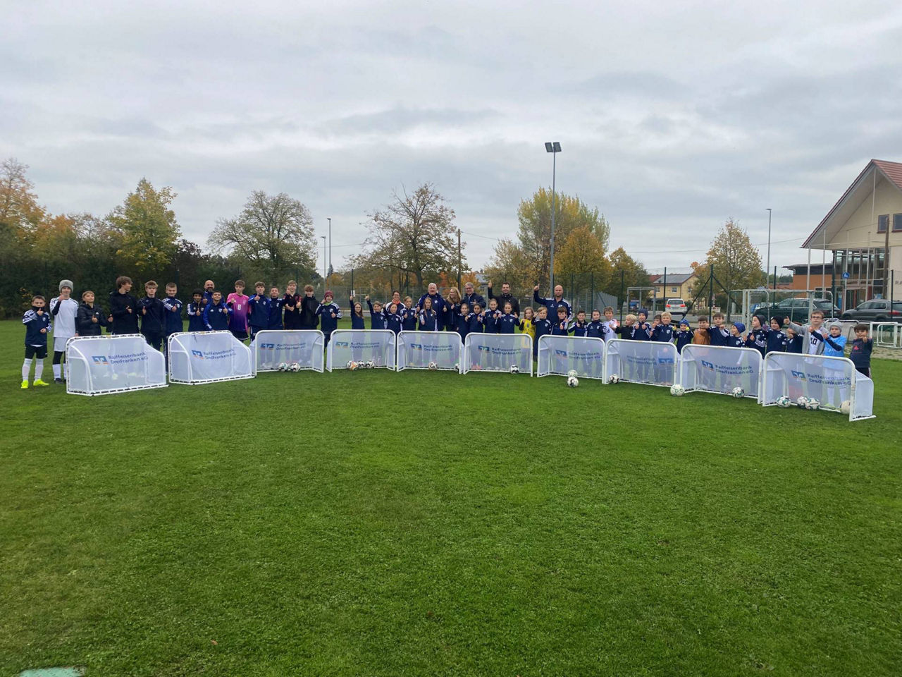 Glückliche Kinder in Fußballtrikots stehen um Kleinfeldtore herum.