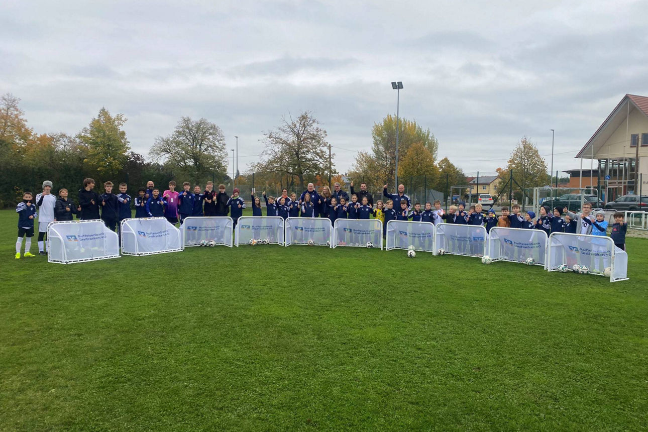 Glückliche Kinder in Fußballtrikots stehen um Kleinfeldtore herum.