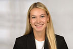 Frau mit blonden langen Haaren. Sie trägt ein weißes Top, einen schwarzen Blazer und goldene Ohrringe