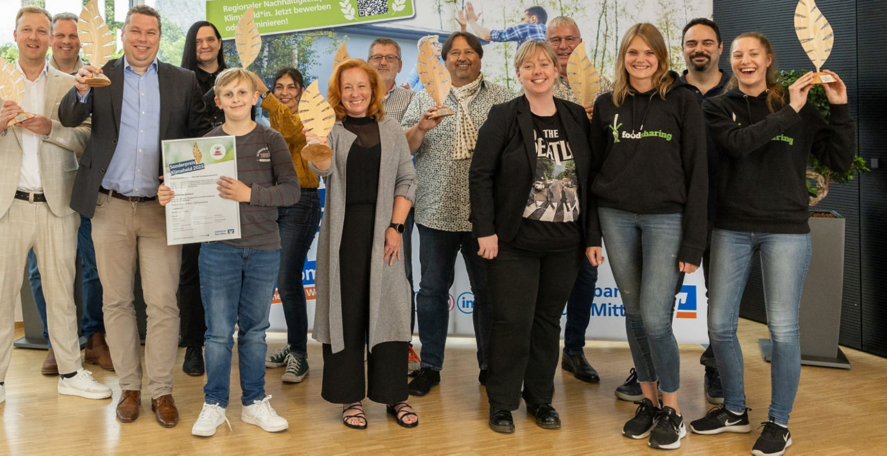 Sieger des regionalen Klimaheldenpreises sind als Gruppe vor einer Pressewand aufgestellt und halten ihre Ehrenpreise in die Kamera.