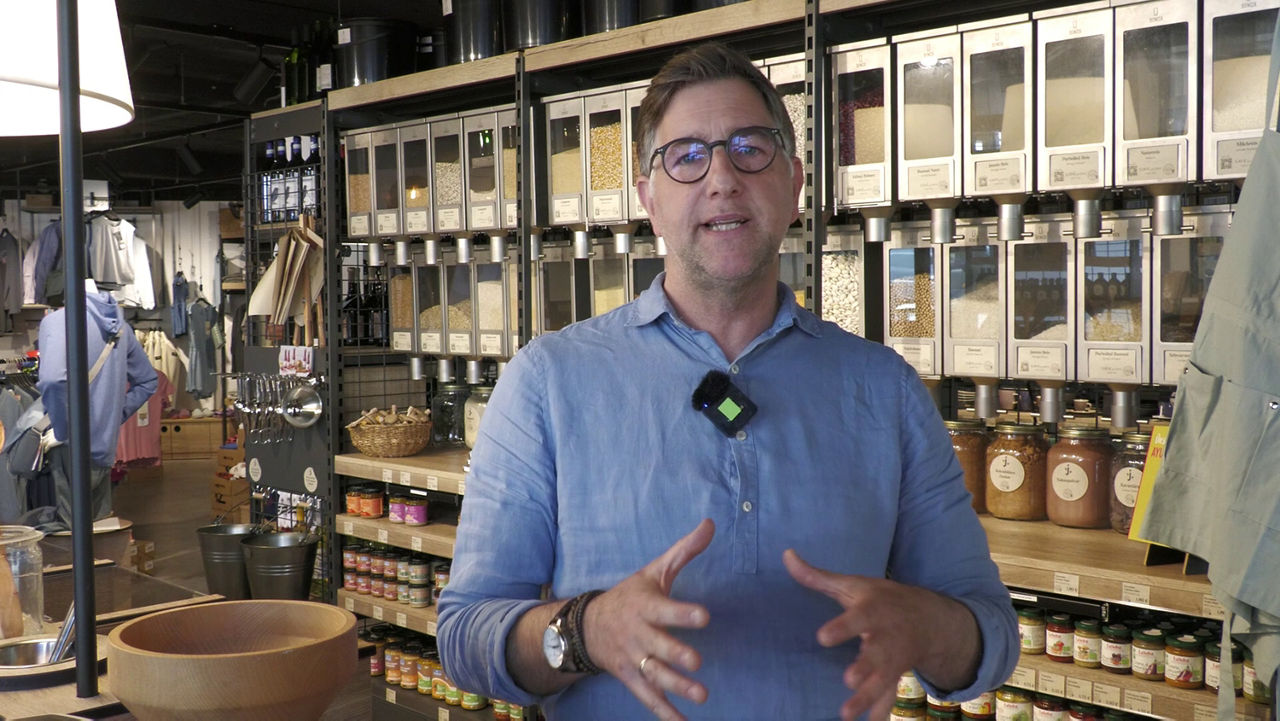 Herr Walter vom Nachhaltigen Einzelhandel "Juut" steht in seinem Verkaufsraum vor einer Wand aus unverpackten Lebensmitteln, die in Glasbehältern präsentiert werden. Er belegt mit seiner Firma beim Klimahelden 2024 den zweiten Platz.