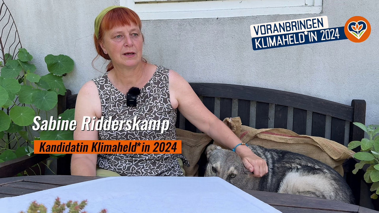 Unsere Gewinnerin des Nachhaltigkeitspreises Klimaheld:in 2024 Sabine Ridderskamp sitzt zusammen mit ihrem Hund auf einer Holzbank in ihrem Garten und streichelt dem Hund über den Kopf. Vor sich ist ein Tisch mit einer kleinen weißen Tischdecke. 