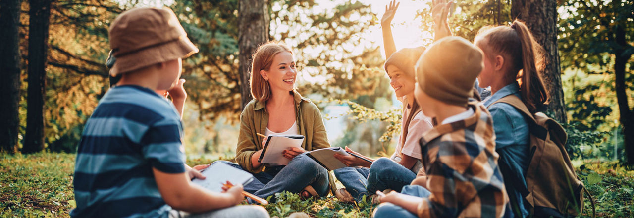 Eine Gruppe lächelnder Kinder und ihr Lehrer sind in einem Wald versammelt