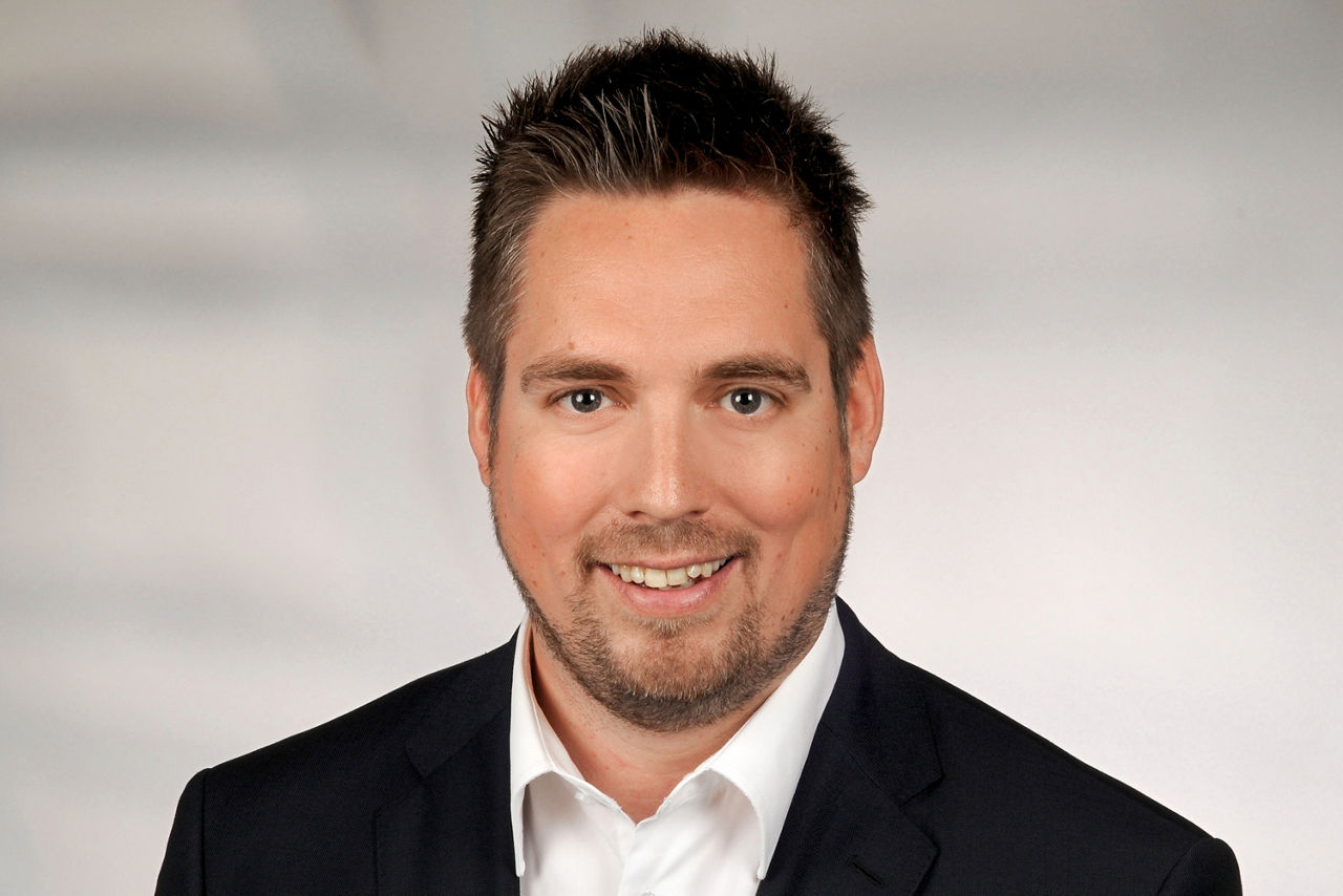 Marc Klimek hat braune kurze Haare, einen leichten Bart und trägt einen Anzug.