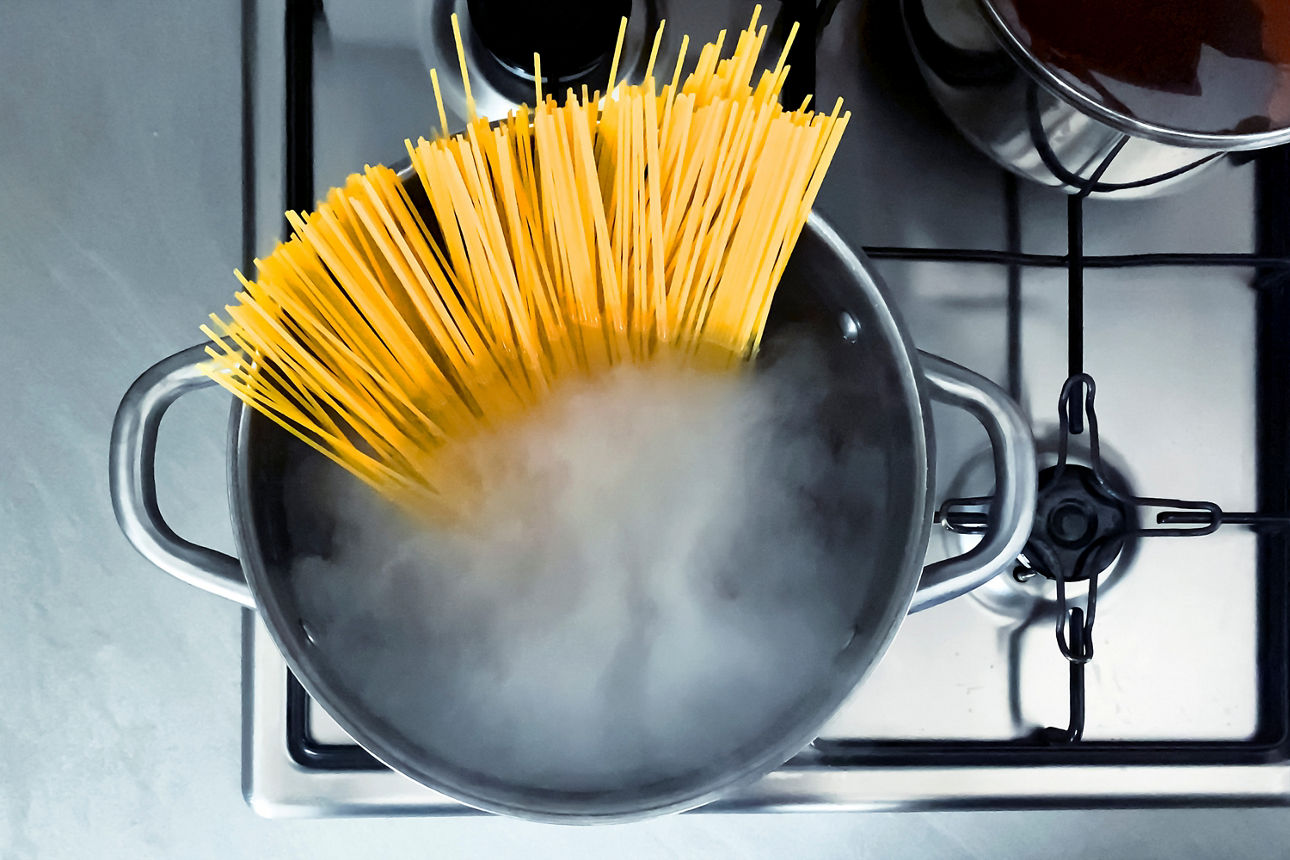Edelstahlkochtopf mit noch ungekochten Spaghetti von oben fotografiert auf Gasherd