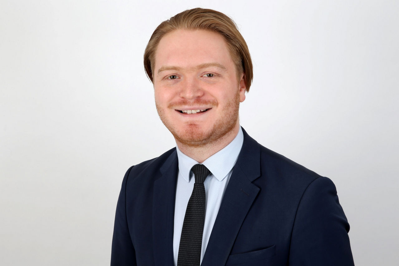 Ein lächelnder Mann in einem Anzug schaut in die Kamera.