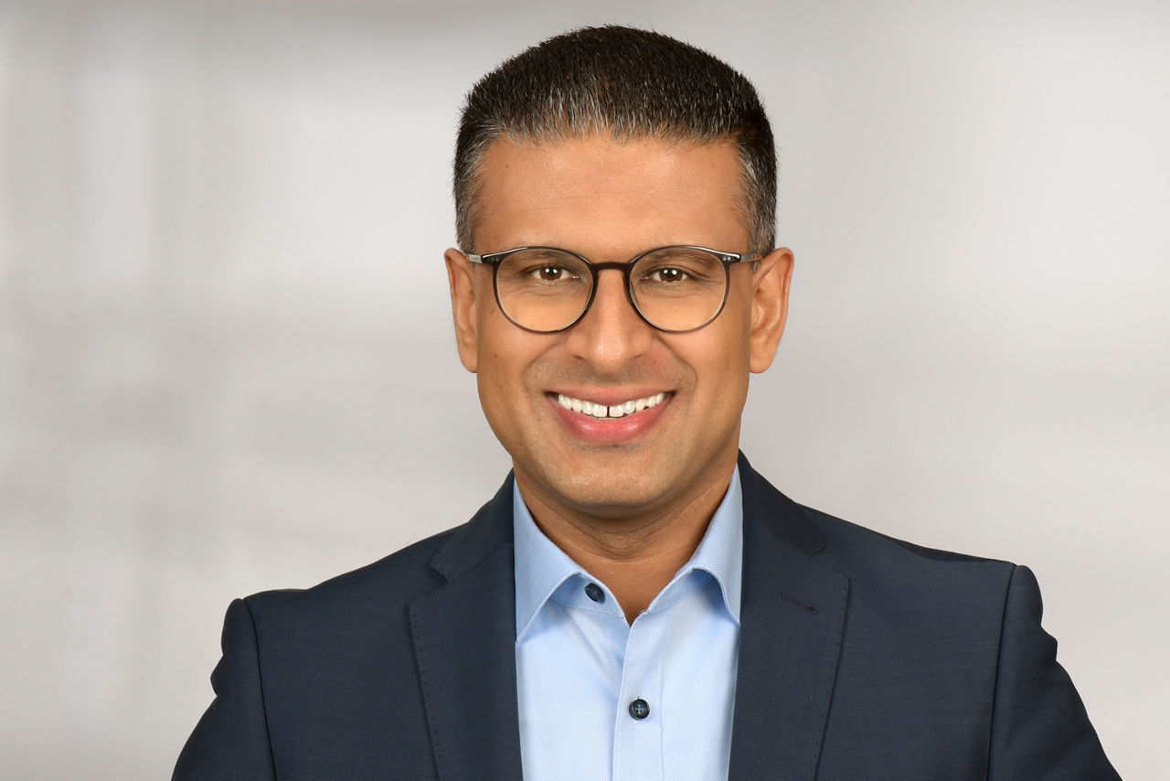 Oberkörperaufnahme einer Person in dunklem Sakko und hellblauem Hemd vor hellem Hintergrund