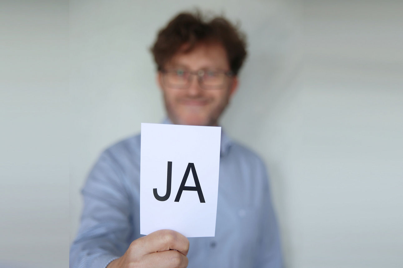 Mitarbeiter mit einem Zettel in der Hand auf dem "Ja" steht.