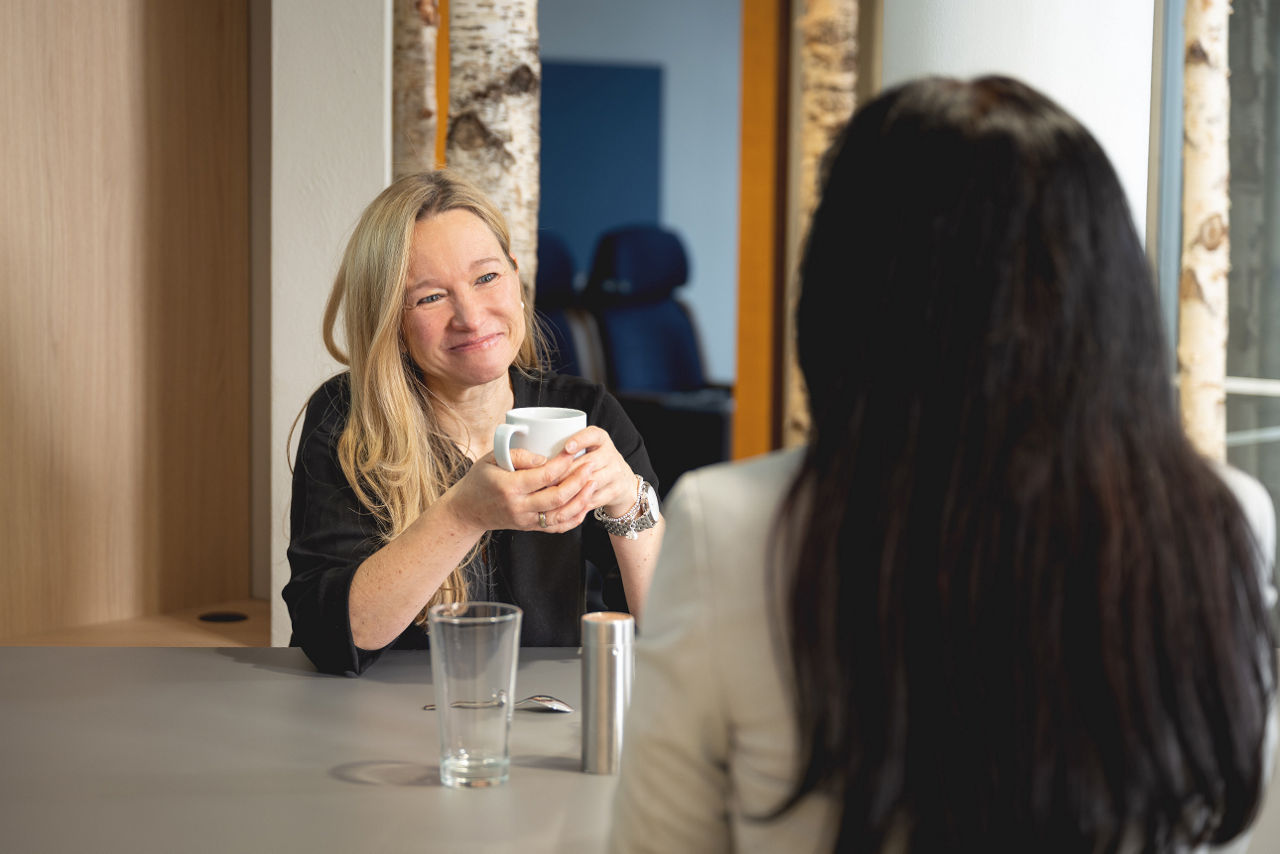 Zwei Frauen sitzen an einem Tisch, trinken Kaffe und unterhalten sich ausgelassen