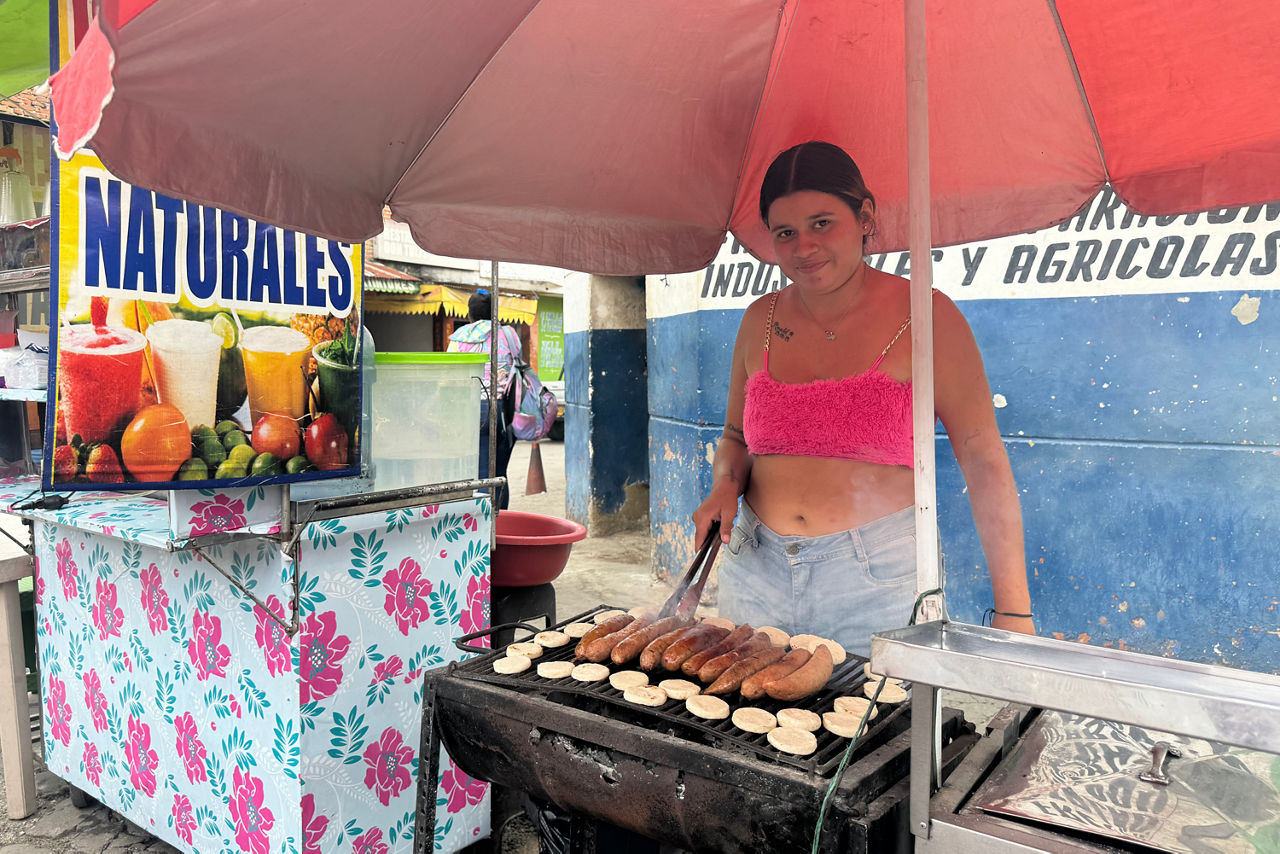 Frau steht an ihrem Straßenstand und grillt Fleisch