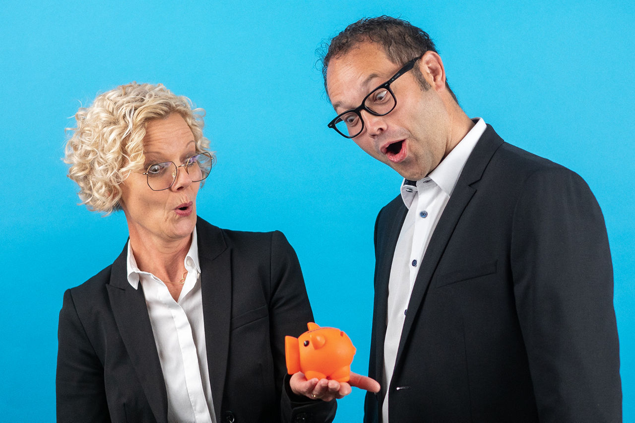 Mann und Frau schauen staunend auf ein orangenes Sparschwein