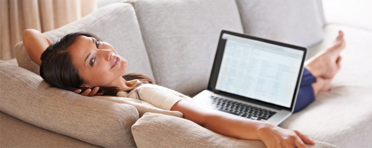 Lachende Frau auf dem Sofa mit einem Laptop auf den Schoss