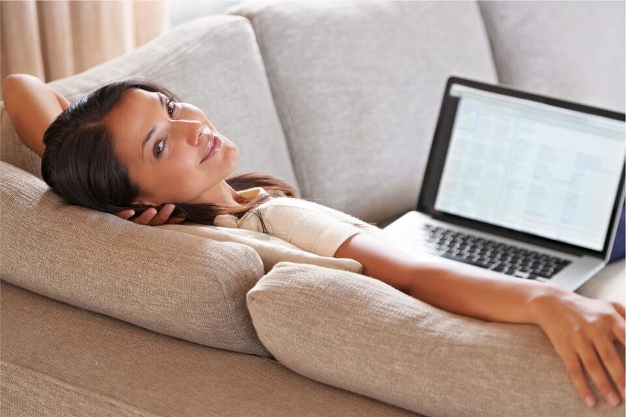 Lachende Frau auf dem Sofa mit einem Laptop auf den Schoss