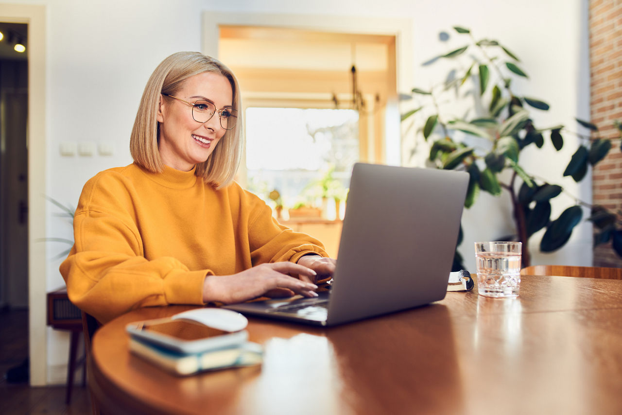 Frau sitzt am Tisch und betreibt Online-Banking