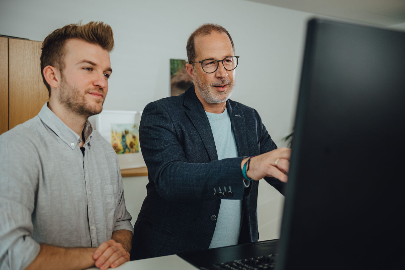 Zwei Mitarbeitende stehen vor einem Computer 