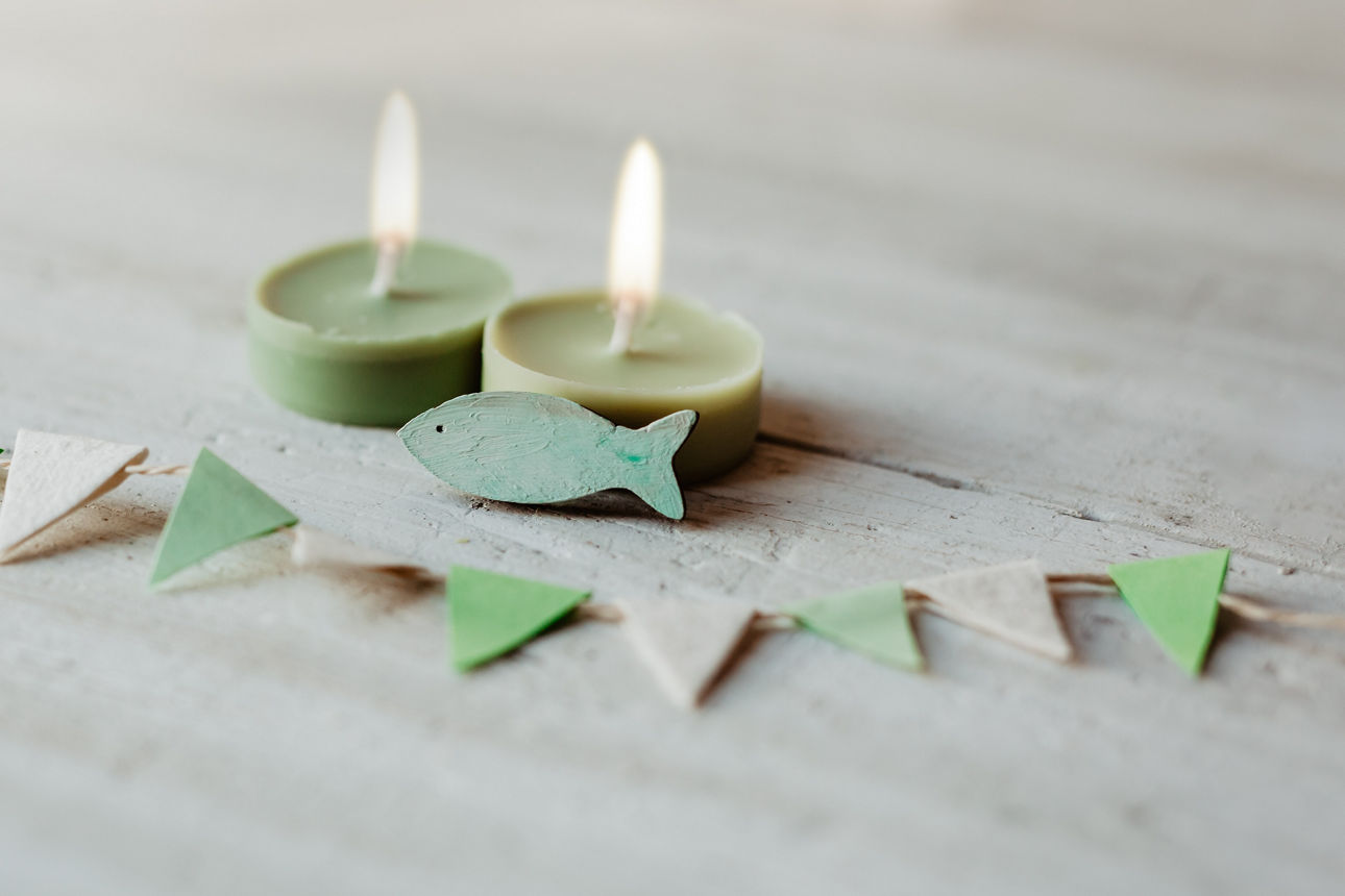 Kommunion, Konfirmation, Firmung, Taufe - Fisch aus Holz auf weißem Holz vor grünen Teelichtern mit Wimpel Girlande