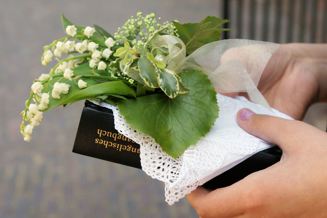 Mädchenhand hält Gesangsbuch und Blumenstrauß