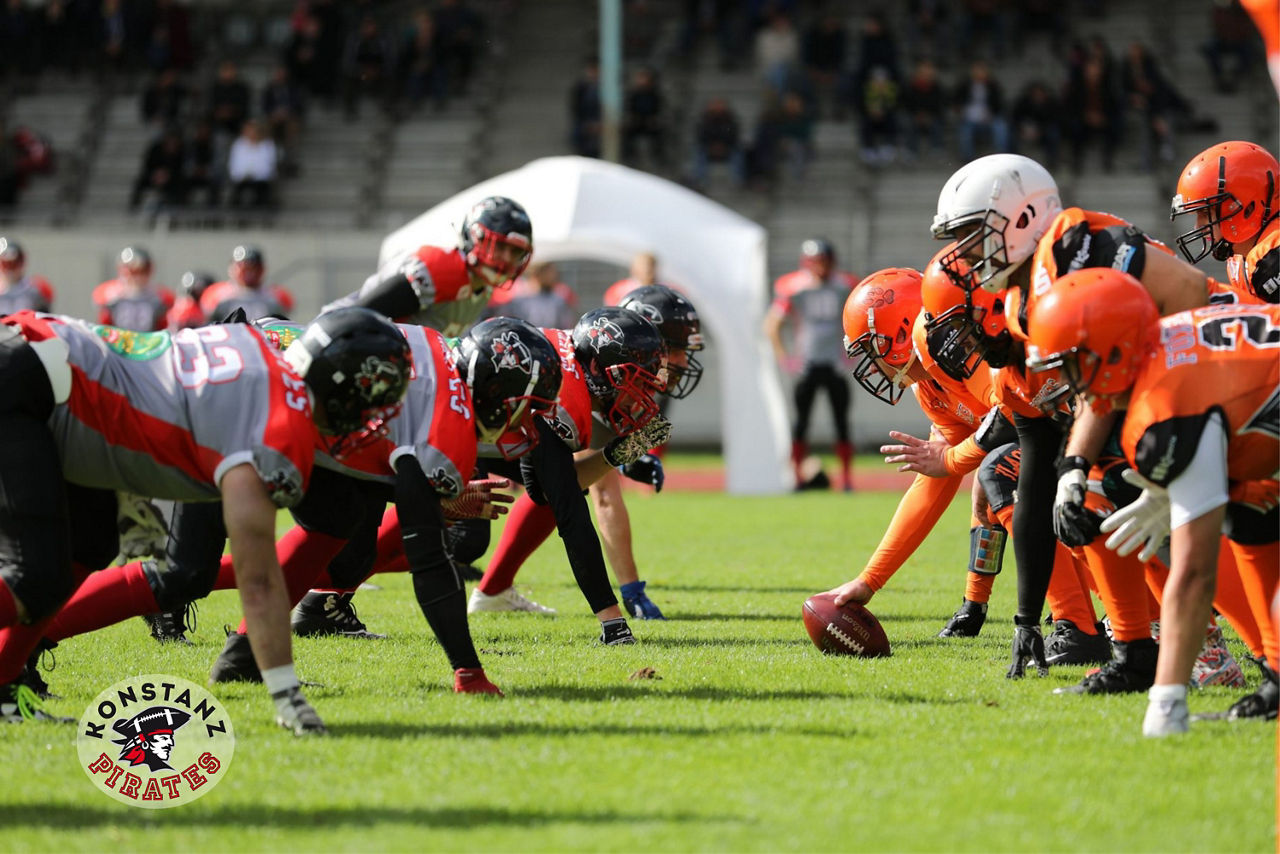 Zwei Football-Teams stehen sich gegenüber. Links ist das Logo der Konstanz Pirates zu sehen.