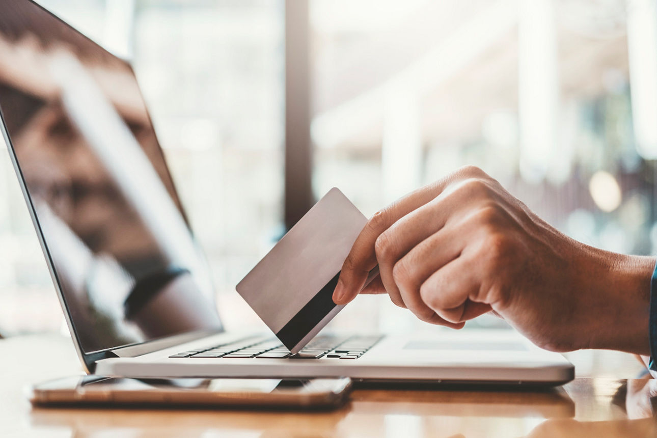 Person hält Girocard in der Hand und sitzt vor einem Laptop