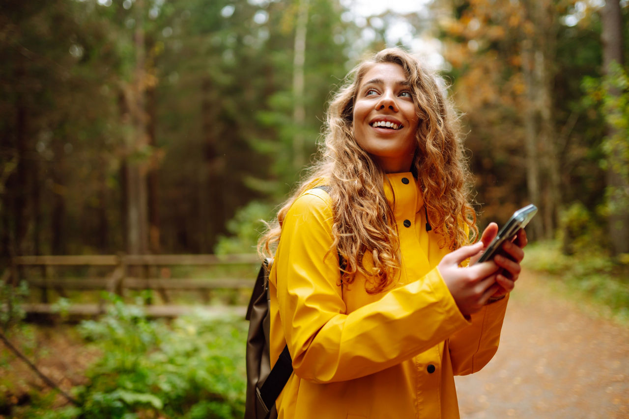 Junge Frau steht mit ihrem Handy in der Hand im Wald.