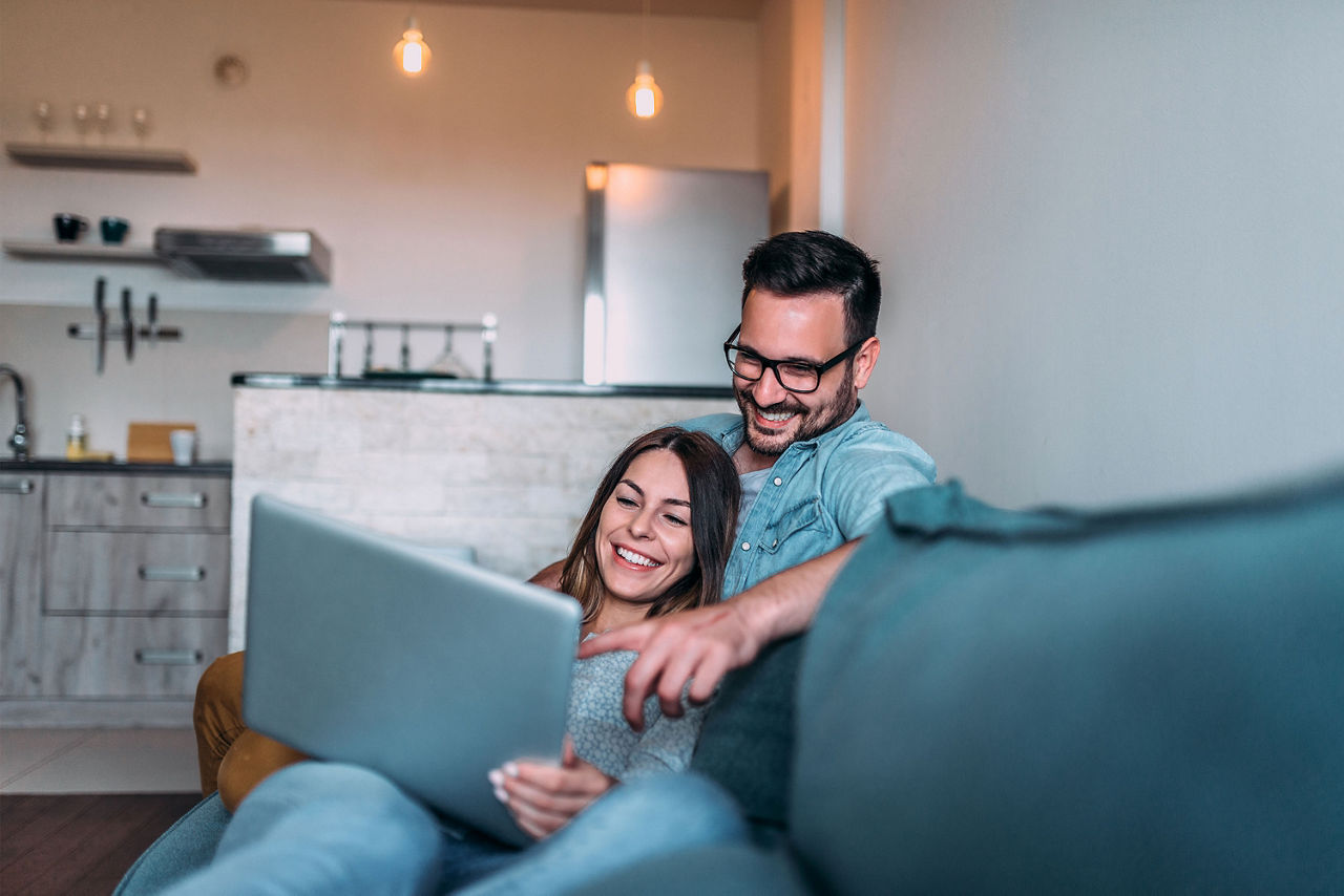 Kuschelndes Paar mit Laptop sitzt auf dem Sofa