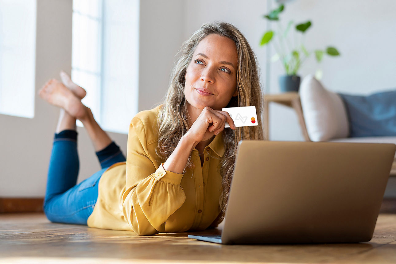 Abbildung zeigt eine blonde Dame, welche mit ihrem Laptop auf dem Fußboden liegt und ihre girocard in der Hand hält.