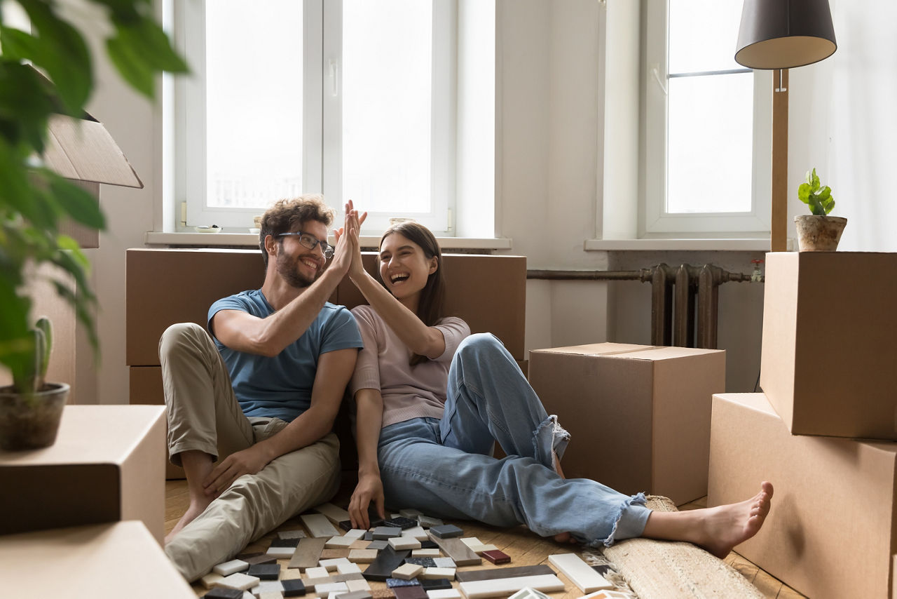 Fröhliches, aufgeregtes junges Paar plant Renovierung nach dem Einzug in die neue Wohnung und  klatscht in die Hände bei Pappkartons