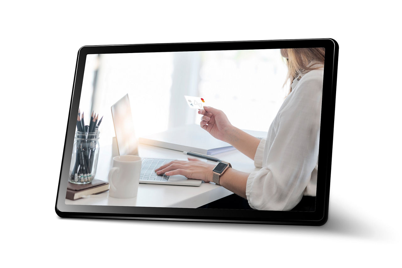 Abbildung zeigt ein Tablet in welchem eine Frau abgebildet ist, die Bankgeschäfte am Laptop tätigt.
