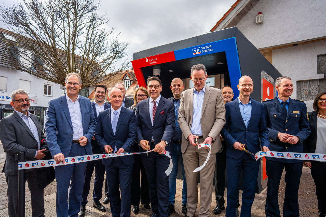 Vor unserer Filiale in Berg stehen Vorstand der Sparkasse und der VR Bank und durchschneiden ein Band.