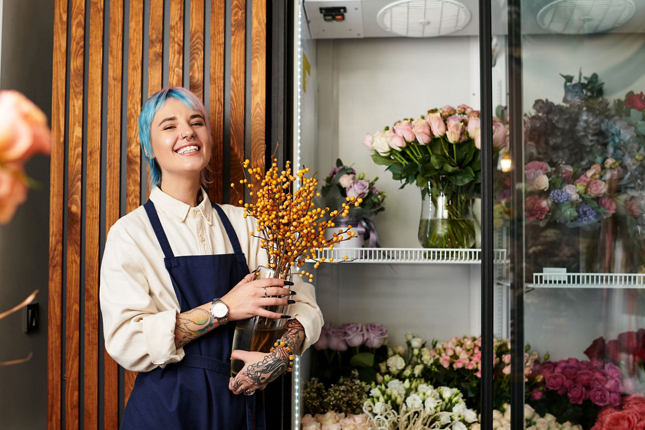 Eine Floristin steht mit einem Strauß Blumen in ihrem Laden und lächelt.