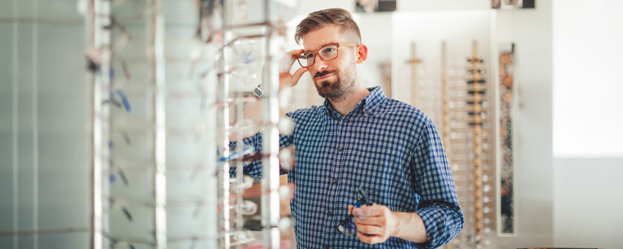 Mann steht im Brillengeschäft und schaut eine Brille an.