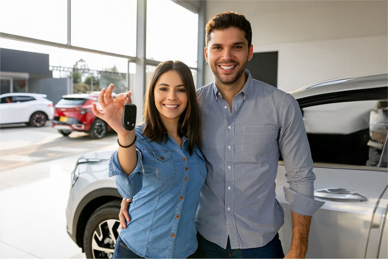 Junges Ehepaar in einem Autohaus bei der Schlüsselübergabe