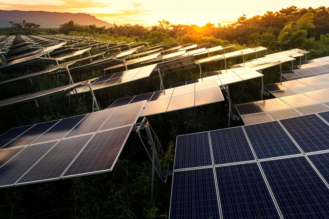 Große Fläche mit Photovoltaikanlagen und Sonnenuntergang im Hintergrund