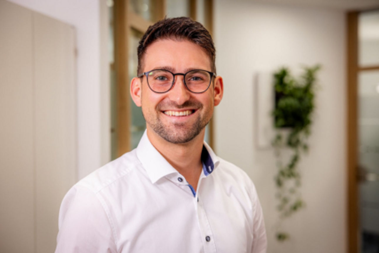 Ein Mann mit Brille und Hemd lächelt in die Kamera.
