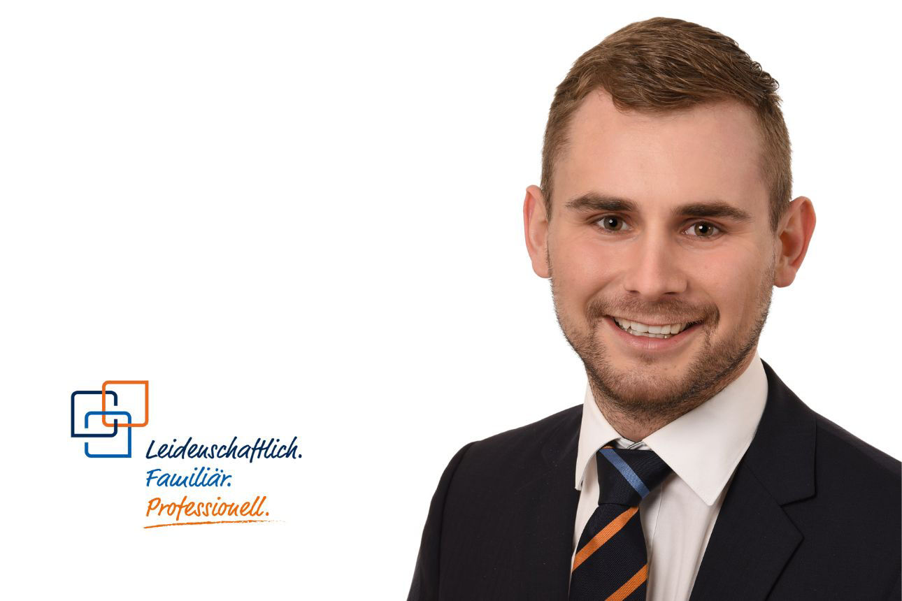 Anton Kreidl, lächelnd, mit kurzen Haaren und einer Krawatte in Dunkelblau und Orange gestreift.