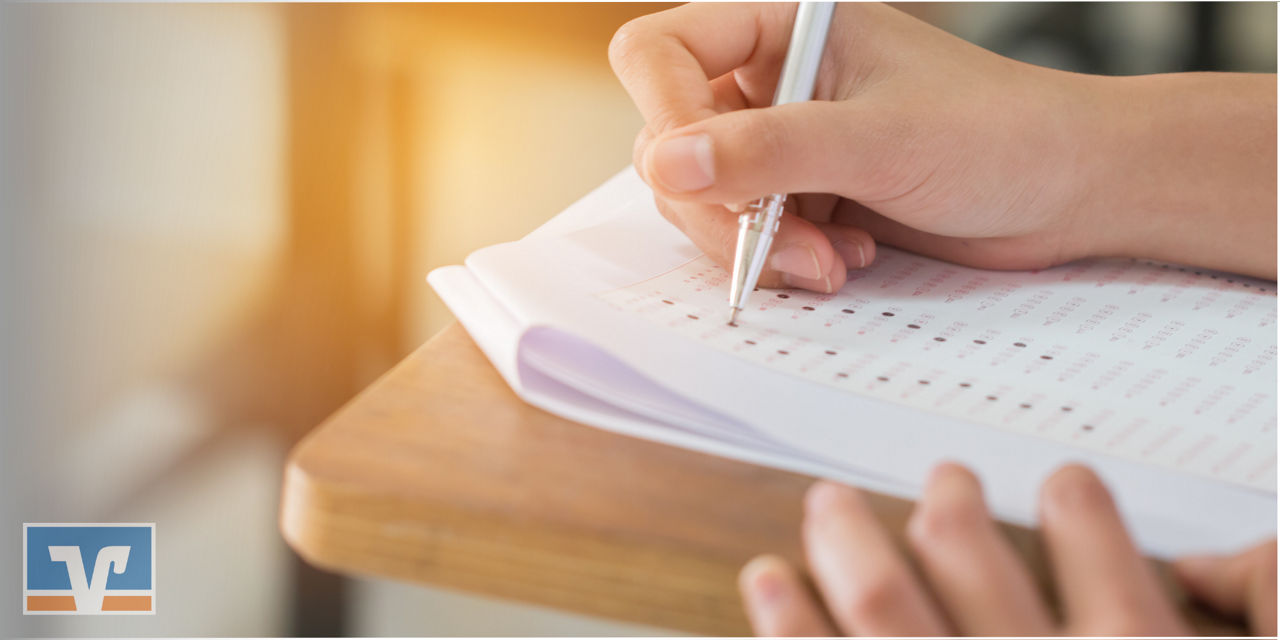 Hand füllt Prüfungsblatt auf Holzschreibtisch aus. 